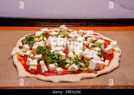 Ungekochter Käse und Basilikum-Pizza auf einer Blechpfanne, die zum Kochen vorbereitet wird Stockfoto