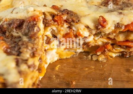 Gebackene Lasagne in einer Glaspfanne, serviert auf weißem Teller mit Gabel und Serviette auf Holzoberfläche Stockfoto