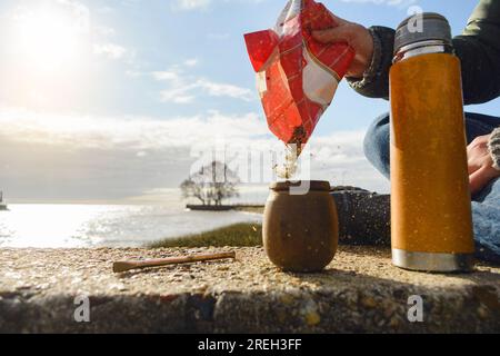 Nahaufnahme einer nicht erkennbaren Person, die morgens auf dem Pier sitzt und den Partner vorbereitet, mit dem Himmel und dem Pier im Hintergrund, bei Sonnenaufgang. Stockfoto