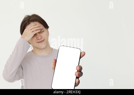 Verwirrter junger Erwachsener, der ein leeres Handy mit leerem weissem Bildschirm und Modell-Banner zeigt Stockfoto