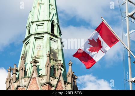 Kanadische Flagge mit blauem Himmel und Kirchturm auf dem Dach des Gebäudes der kanadischen Botschaft in Riga, Lettland Stockfoto