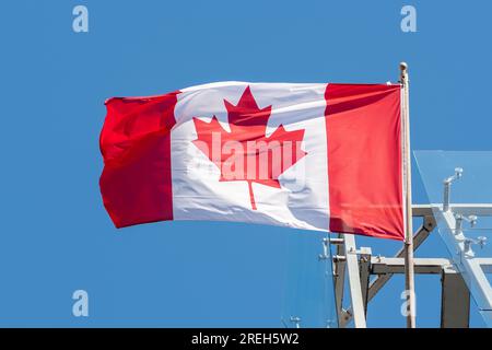 Die Flagge Kanadas, die in der Sonne mit blauem Himmel auf dem Hintergrund wartet, aus nächster Nähe Stockfoto