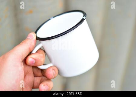 Weißer, metallemaillierter Becher in den Händen einer Person Stockfoto