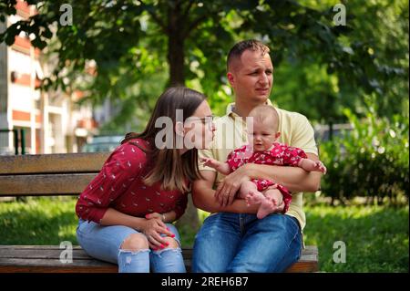 Eine Familie mit einem kleinen Mädchen, das auf einer Bank im Park sitzt Stockfoto