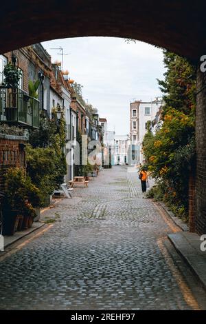 Mews in Notting Hill durch einen Bogen, eine Dame geht davon Stockfoto