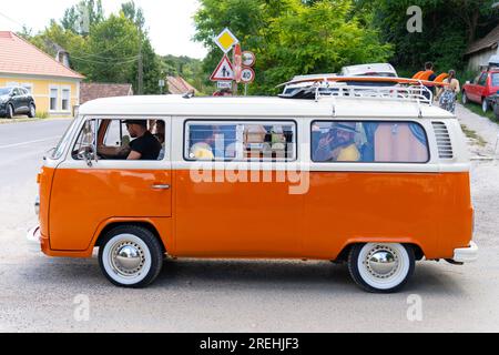 Orangefarbener alter Volkswagen Transporter Minibus mit winkenden Touristen. Valley of Arts Festival in Kapolcs, Ungarn. Juli 27. 2023. Stockfoto