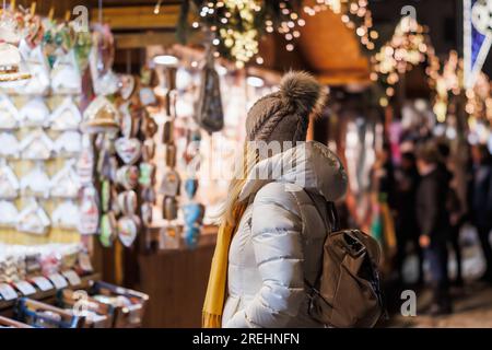 Eine Frau mit Strickmütze, die auf dem weihnachtsmarkt nach Souvenirs sucht. Weibliche Touristen genießen Winterurlaub in der Stadt Stockfoto