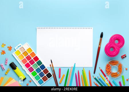 Aquarell, Pinsel auf blauem Hintergrund. Flach liegend, Draufsicht. Kreativer Künstler Arbeitsplatz, Modell. Tisch mit leerem Skizzenbuch, Bleistiften, Farbpalette. Schmerzen Stockfoto