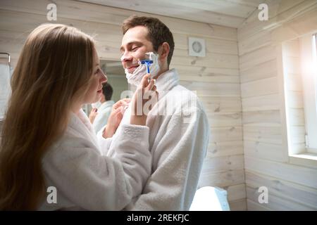 Junger Mann und junge Dame, die in der Badewanne stehen, Frau, die Männergesicht rasiert Stockfoto