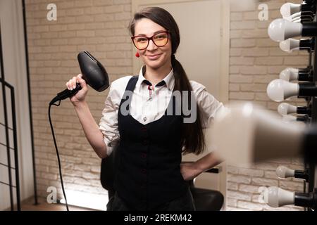 Lächelnde Frau in Brille mit Fön Stockfoto