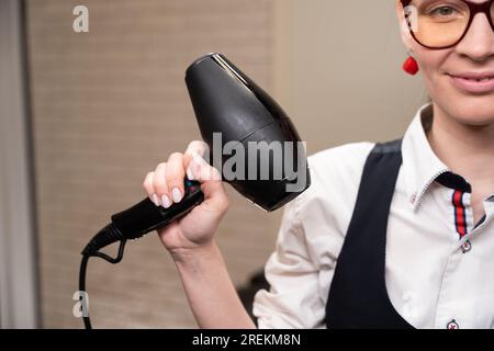 Eine Frau mit Brille hält einen Fön in der Hand Stockfoto