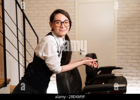 Eine Frau mit Brille steht am Friseurstuhl Stockfoto