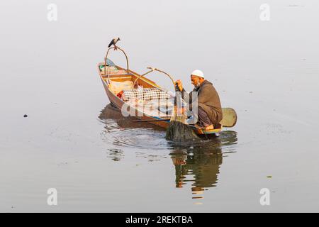 Dal Lake, Srinagar, Jammu und Kaschmir, Indien. 26. Oktober 2022. Die Krähe beobachtet einen Fischer, der sein Netz auf einem Boot in Lake Dal sammelt. Stockfoto