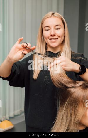 Ein Friseur schneidet einer Blondine die Haare in einem Schönheitssalon. Frauenfrisur Stockfoto