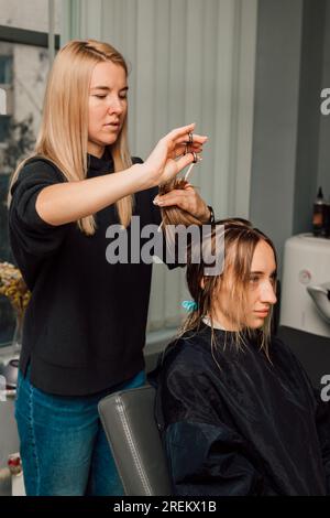 Ein Friseur schneidet einer Blondine die Haare in einem Schönheitssalon. Frauenfrisur Stockfoto