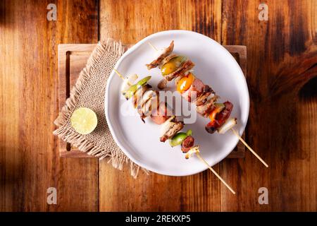 Hausgemachte Spieße mit Fleisch und gegrilltem Gemüse, serviert auf einem rustikalen Holzbrett, auch bekannt als Brochetten, alambre, Chuzo oder Pincho. Tabelle topview. Stockfoto