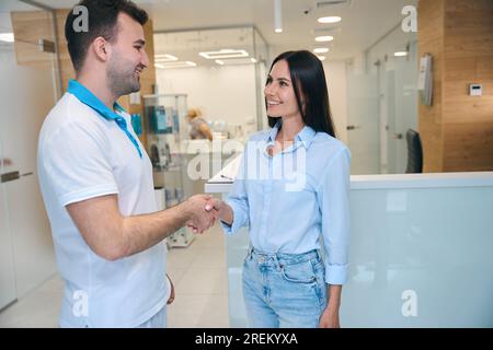 Ein lächelnder Mann begrüßt eine Frau in der Lobby der Klinik Stockfoto