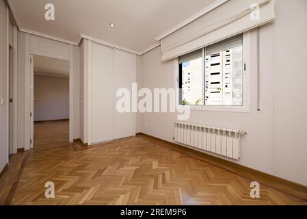 Leerer Raum mit eingebautem Kleiderschrank mit weißen Schiebetüren, einem großen Aluminiumheizkörper unter dem Fenster mit einem Klappdeckel, Putzleisten auf t Stockfoto