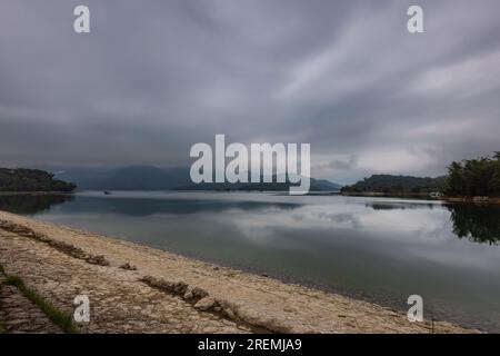 Der wolkige Himmel verleiht dem Sun Moon Lake, Taiwan, eine geheimnisvolle Atmosphäre. Sanftes Licht durchdringt das Wasser und wirft ein ätherisches Licht auf das Wasser. Mitten im Nebel, Stockfoto