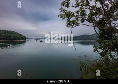 Der wolkige Himmel verleiht dem Sun Moon Lake, Taiwan, eine geheimnisvolle Atmosphäre. Sanftes Licht durchdringt das Wasser und wirft ein ätherisches Licht auf das Wasser. Mitten im Nebel, Stockfoto