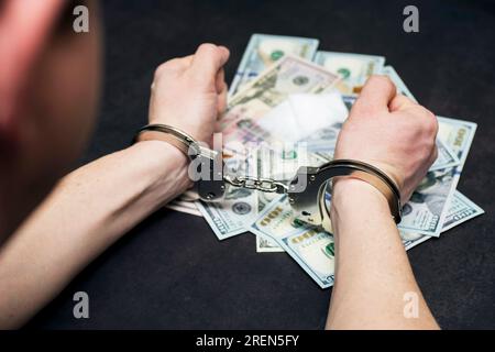 Mann in Handschellen mit Geld und Drogen auf dunklem Hintergrund. Stockfoto