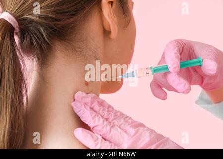 Dermatologe punktiert vom Muttermal einer jungen Frau auf rosa Hintergrund, Nahaufnahme Stockfoto