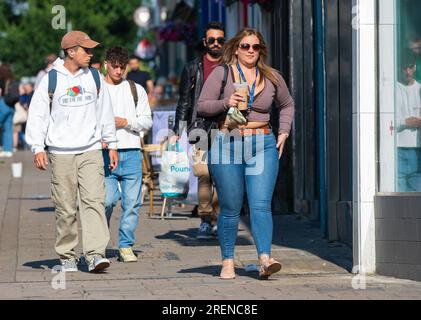 Hübsche junge Frau in Jeans, modisch gekleidet, in der geschäftigen Stadt unterwegs, mit einem Mitnahmegetränk, Schultertasche, im Sommer in Großbritannien. Fußgänger. Stockfoto