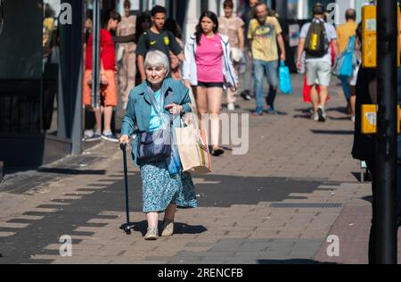 Ältere Dame mit Gehstock oder Gehstock in einer geschäftigen Einkaufsstraße in Brighton & Hove, England, Großbritannien. Stockfoto
