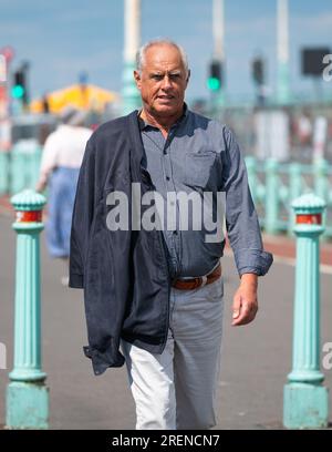 Ein kluger, gut gekleideter Mann in geknöpftem Hemd und Hose, der eine Jacke über der Schulter trägt und im Sommer in Großbritannien entlang einer Strandpromenade spaziert. Stockfoto