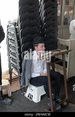 Bei Tisha B'AV Services beobachtet ein junger Mann die trauernden Aspekte des Tages, indem er fastet, auf einem niedrigen Sitz sitzt und keine Lederschuhe trägt. In Rockland. Stockfoto