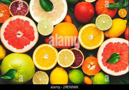 Farbenfrohe Zitrusfrüchte, Essenshintergrund, Draufsicht. Mischung aus verschiedenen ganzen und geschnittenen Früchten: Orange, Grapefruit, Zitrone, Limette und andere mit Blättern Stockfoto