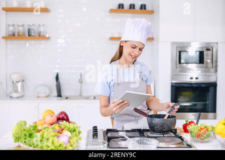 Glückliche Frau Kochen Essen zu Hause Küche lernen gesundes Gemüse Kochen Online-Kurs Internet Video auf Tablet anschauen Stockfoto