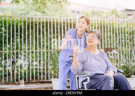 Ältere Erwachsene Frau mit Behinderung in einer häuslichen Krankenschwester oder einem Physiotherapeuten helfen, sich im Freien zu entspannen Stockfoto