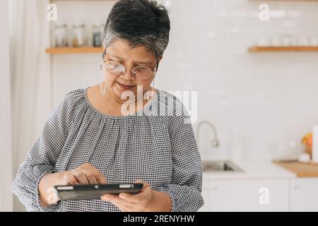 Eine ältere asiatische Frau lernt, moderne Technik zu verwenden. Mutter versucht, mit dem Tablet-PC über den Touchscreen zu kommunizieren Stockfoto