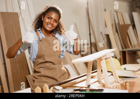 Glückliche Zimmerlerin afrikanische Schwarze, die in der Holzwerkstatt lächelt, machen gerne handgefertigte Holzmöbel. Stockfoto