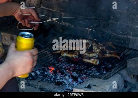 Mann mit Bierdose, der Hühnerflügel grillt Stockfoto