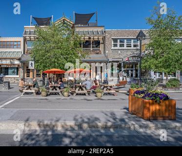 Banff, Alberta, Kanada – 27. Juli 2023: Die Menschen essen an Picknicktischen in der Banff Avenue Stockfoto