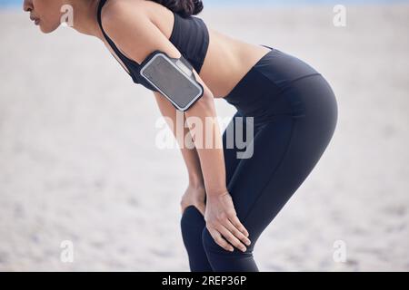 Frau, Fitness und Pause am Strand nach Workout, Lauftraining oder Outdoor-Kardio-Training. Hände und Körper fit, aktive und sportliche Frau Stockfoto