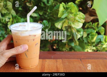 Hand hält eine Tasse leckeren Thai-Eistee auf dem Gartentisch Stockfoto