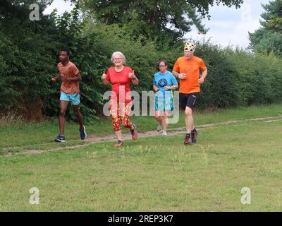 Kesgrave, Suffolk - 29. Juli 2023 : warmer Sommer am Samstagmorgen Parkrun im Millennium Field. Daumen hoch und ein Lächeln von einer Seniorin in roter Ausrüstung. Stockfoto