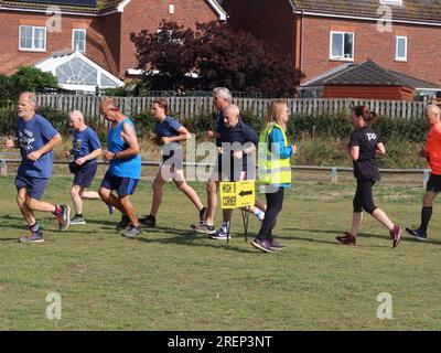 Kesgrave, Suffolk - 29. Juli 2023 : warmer Sommer am Samstagmorgen Parkrun im Millennium Field. Die Gruppe fährt am Marshal an der Ecke High 5 vorbei. Stockfoto