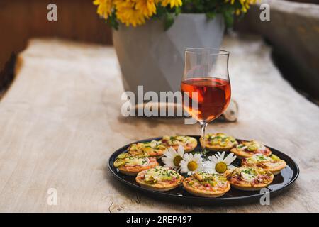 Ein kleiner Imbiss, Pizzas Piccolo auf schwarzem Teller mit einem Glas Wein, auf einem Holztisch Stockfoto