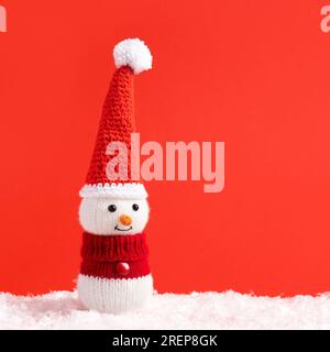 Gestrickter Schneemann mit rotem Weihnachtsmütze. Frohe Weihnachten und Neujahr 2024 Grußkarte. Babyspielzeug. Geschenk für die Winterferien. Stockfoto