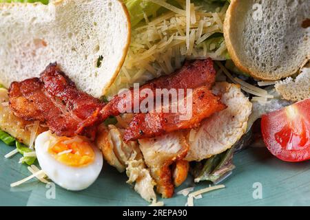 Salat Caesar mit Speck, Huhn, Gemüse, Ei und Croutons, Nahaufnahme auf einem Teller. Seitenansicht Stockfoto