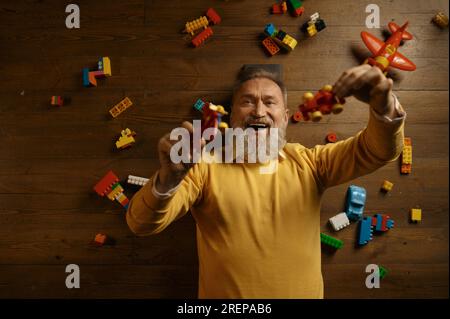 Blick von oben auf einen älteren Mann, der auf dem Boden liegt und Spielzeug spielt Stockfoto