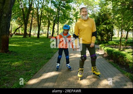 Glücklicher Seniorenmann und kleiner Junge beim Rollschuhlaufen im Stadtpark Stockfoto