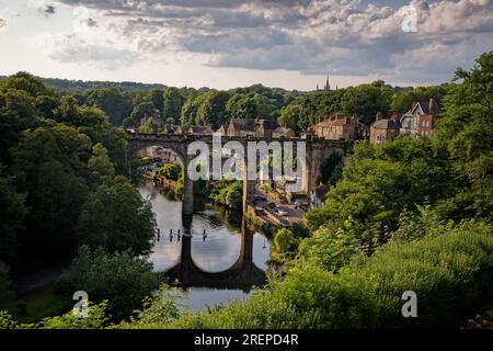 Abendlicht taucht die Stadt und die bewaldete Nidd Gorge in Knaresborough mit Paddleboardern auf dem Fluss in North Yorkshire, England. Stockfoto