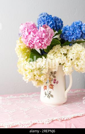 Wunderschöner Sommerstrauß mit rosa, lila und weißen Hortensien in einer Vase, gemütliche Inneneinrichtung, Tisch mit pinkfarbener Tischdecke und Blumenstrauß Stockfoto