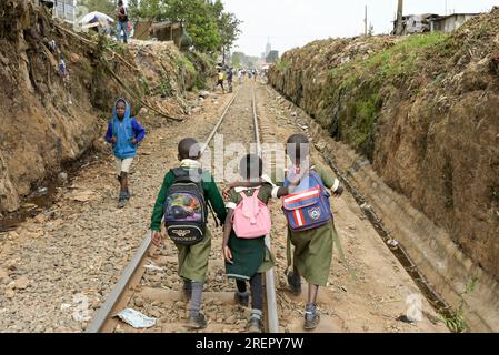 KENIA, Nairobi, Slum Kibera, Schüler mit Tornister, die von der Schule nach Hause laufen auf der Kibera Eisenbahnstrecke / KENIA, Nairobi, Slum Kibera, Kinder gehen nach der Schule nach Hause an der Kibera Bahnlinie Stockfoto