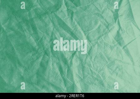 Zerknitterter, zerknitterter grüner Textilhintergrund. Zerknitterte und geknickte abstrakte Kulisse aus Spinnvlies, Tapete mit Kopierbereich, Draufsicht. Stockfoto